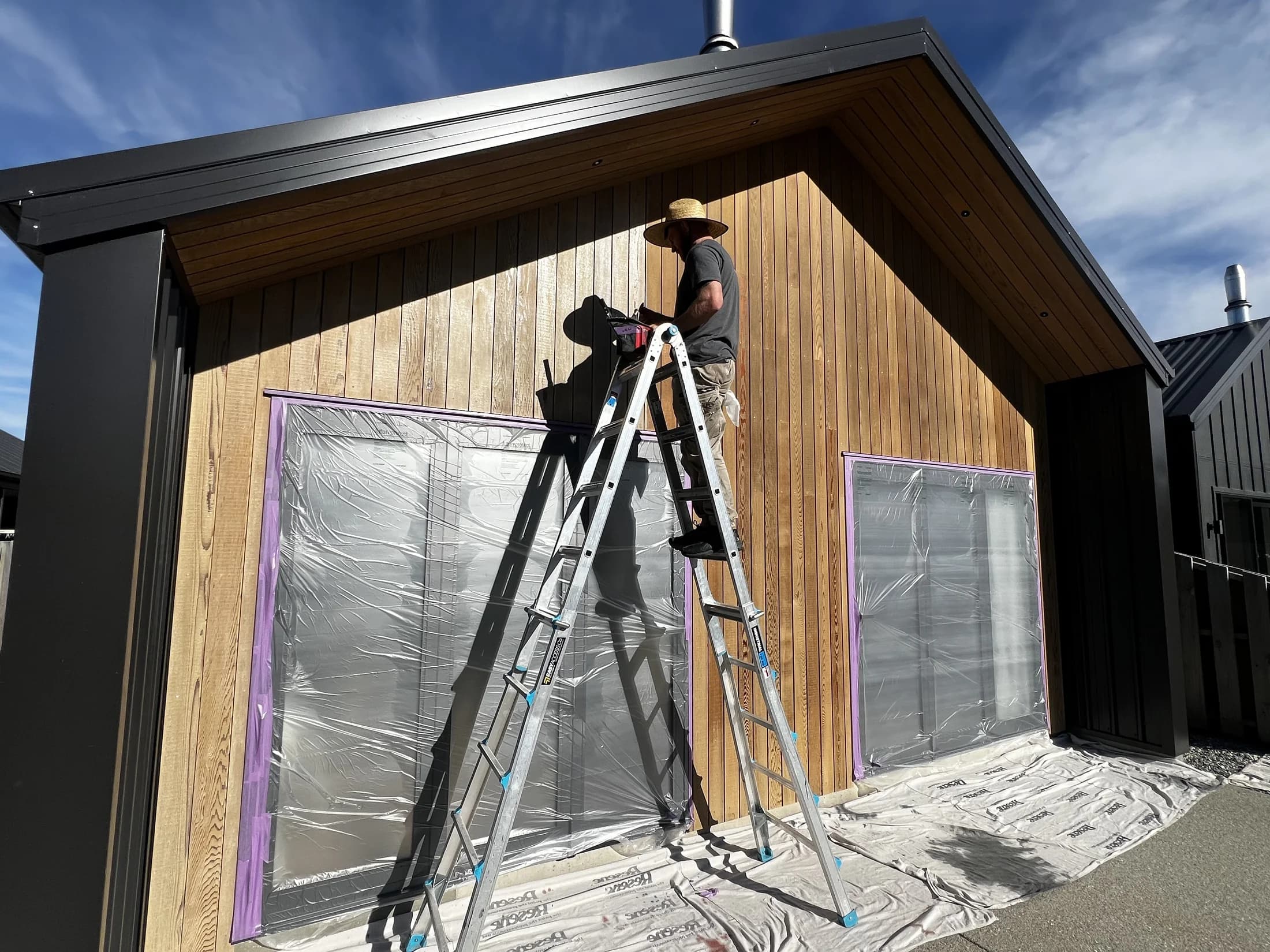 Painter on a ladder oiling cedar weatherboard cladding in Wanaka