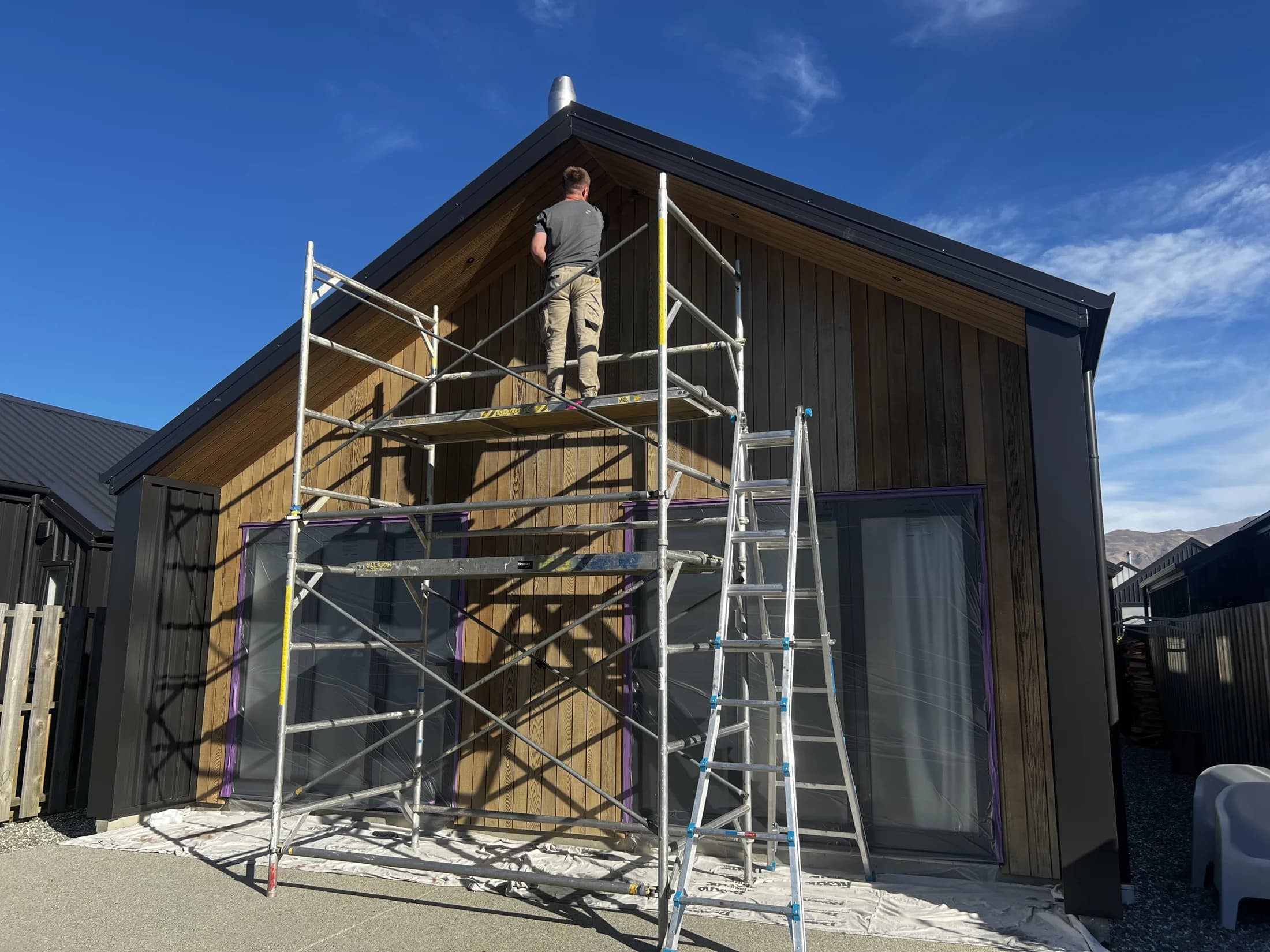 Applying cedar oil stain from a scaffold in Northlake, Wanaka